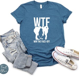 May include: A teal blue t-shirt with a white graphic of two hockey players facing off with the text "WTF WIN THE FACE-OFF".