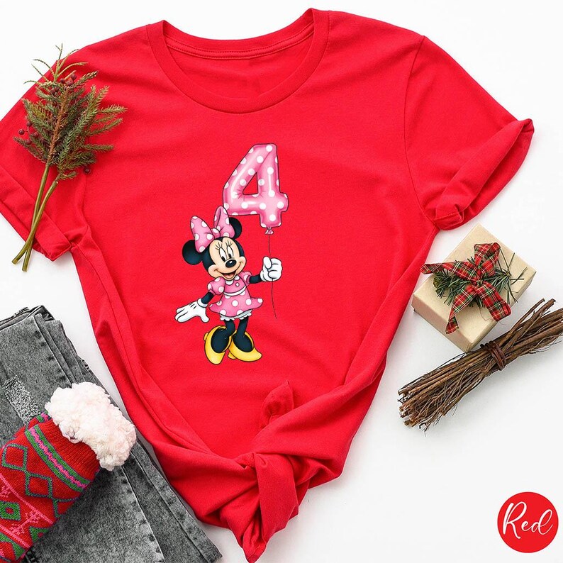 K&ouml;nnte beinhalten: Ein rotes T-Shirt mit einer Minnie Mouse-Grafik, die einen rosa Ballon mit der Zahl 4 h&auml;lt. Minnie Mouse tr&auml;gt ein rosa gepunktetes Kleid und eine Schleife. Das Wort "Red" befindet sich in einem Kreis unten rechts.
