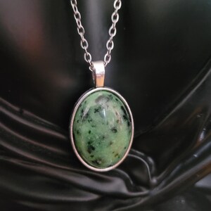Peut inclure: Un collier argenté avec un pendentif ovale. Le pendentif présente une pierre verte avec des mouchetures noires, sertie dans un cadre argenté. La chaîne est de style maillon délicat, adaptée au quotidien.