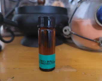 May include: A small, brown glass bottle with a black cap. The bottle has a teal label with the words "Firey Wall Protection" in white. The bottle is on a wooden surface, with a blurred background featuring a cauldron and other objects.