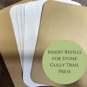 May include: A stack of white paper refills for a Stone Gully Trail press. The top sheet has a green circle with the text "INSERT REFILLS FOR STONE GULLY TRAIL PRESS".
