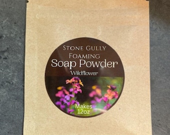 May include: A kraft paper packet of Stone Gully Foaming Soap Powder, Wildflower scent. The circular label features a floral image and text that reads "Makes 12oz". The packet is sealed at the top.