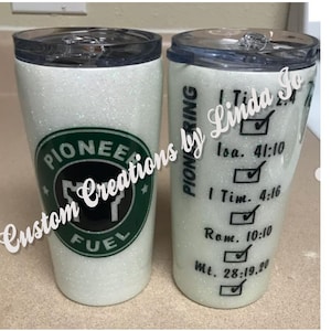 Könnte beinhalten: Zwei weiße Glitzerbecher mit schwarzer Beschriftung. Ein Becher hat einen grünen Kreis mit dem Text "Pioneer Fuel" und eine Kuhsilhouette. Der andere Becher hat den Text "Pioneering by Linda So" und eine Liste von Bibelversen mit Häkchen.