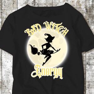 May include: Black t-shirt with a yellow graphic of a witch flying on a broomstick in front of a full moon. The text "Bad Witch Energy" is written in a gothic font.