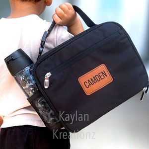 May include: Black lunch bag with a brown leather patch that says "CAMDEN". The bag has a mesh side pocket and a zipper closure.