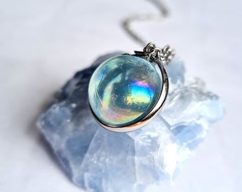May include: A silver chain necklace with a round iridescent blue gemstone pendant. The pendant is set in a silver bezel and has a rainbow sheen.