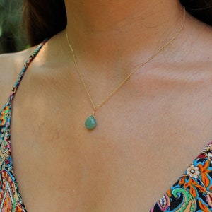 Peut inclure: Un collier en chaîne dorée avec un pendentif en forme de larme vert clair. Le collier est porté par une personne avec un haut à motifs.