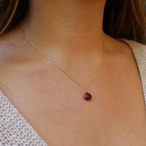 Puede incluir: Un collar de cadena de oro con un pequeño colgante de rubí en forma de lágrima.