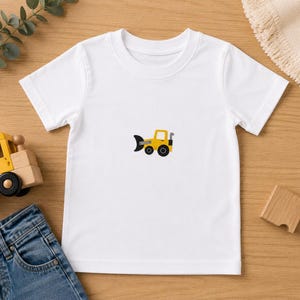 May include: A white short-sleeved t-shirt featuring a small, centered graphic of a yellow construction bulldozer with black wheels and a black blade. The shirt has a classic crew neckline and a plain, solid white fabric construction throughout.