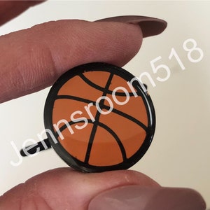 May include: A black and orange basketball charm with a black ring attached.