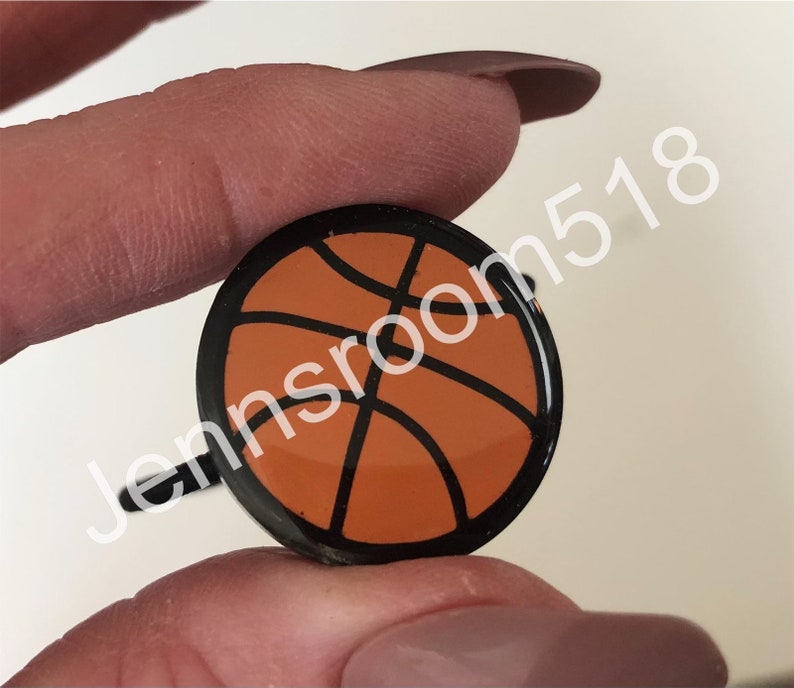 May include: A black and orange basketball charm with a black ring attached.