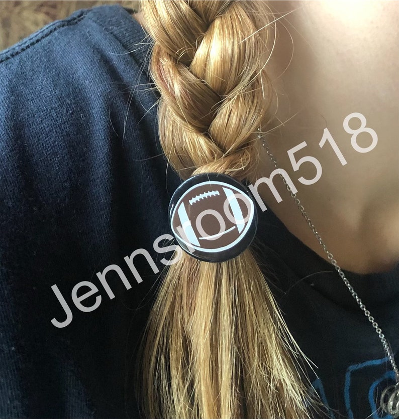 May include: A black and white football design button is used as a hair tie on a blonde braid.