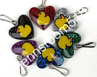 May include: Seven heart-shaped zipper pulls with glitter and a rubber ducky charm. Each zipper pull is a different colour: red, silver, green, purple, blue, black, and gold.
