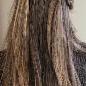May include: A person with long brown hair with blonde highlights wearing two black hair ties with yellow softball designs.
