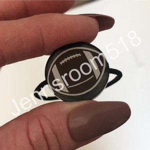 May include: A black hair tie with a round, brown and white football design.