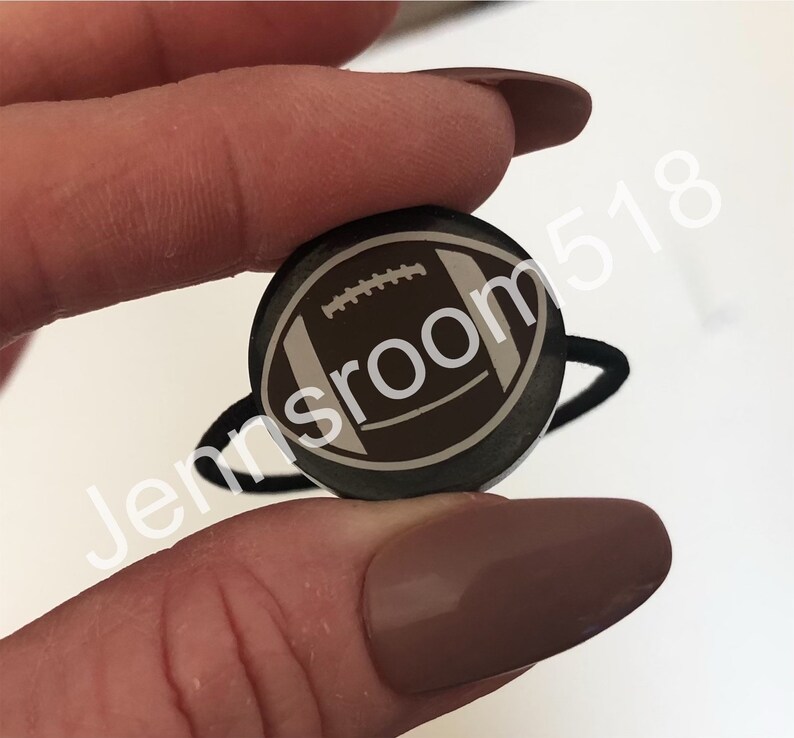 May include: A black hair tie with a round, brown and white football design.