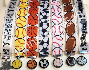 May include: Set of seven colorful bookmarks with different sports ball designs. Each bookmark features a white ribbon with a sports ball pattern and a metal charm with a matching ball design. The charms include a baseball, basketball, football, soccer ball, softball, and volleyball.
