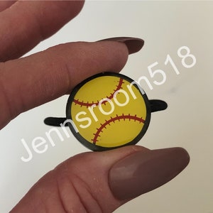 May include: A black and yellow softball charm with red stitching. The charm is attached to a black elastic hair tie.