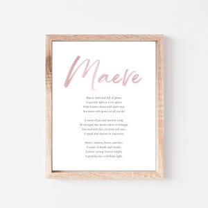 May include: A framed print featuring the name "Maeve" in a soft pink watercolor font. The print includes a poem about the name Maeve in a classic serif font, set against a white background. The frame is a light wood color.