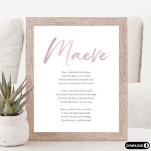 May include: A framed print with the name "Maeve" in a soft pink watercolor font. The print includes a poem about the name Maeve. The frame is a light brown color, and a small succulent plant in a white pot is visible in the foreground.