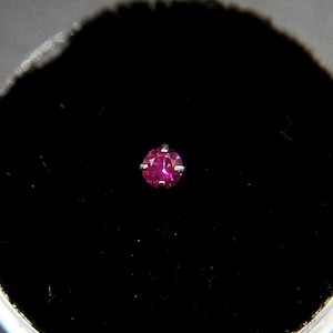 May include: A small, round, pink gemstone set in a silver nose ring.