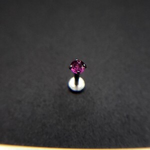May include: A close-up of a small, purple gemstone set in a silver stud earring.