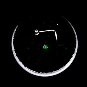 May include: Two nose rings with green gemstones. One ring is a straight stud and the other is a curved L-shaped ring.