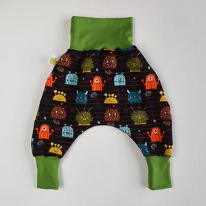 Op de afbeelding: Zwarte en groene babybroek met een monsterprint. De broek heeft een groene omslagband en groene boorden.