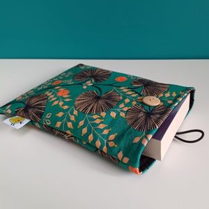 Puede incluir: Una funda de libro verde con un patr&oacute;n floral en tonos naranja, negro y blanco. La funda tiene un cierre de bot&oacute;n y una correa negra.