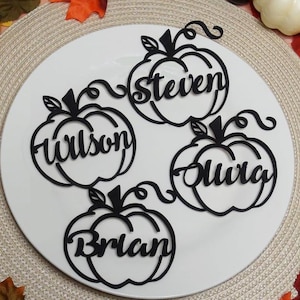 Puede incluir: Cuatro adornos negros con forma de calabaza cortados con l&aacute;ser en material plano. Cada calabaza tiene un nombre recortado en el centro: steven, Wilson, Olivia y Brian. Los adornos tienen tallos y zarcillos rizados en la parte superior.