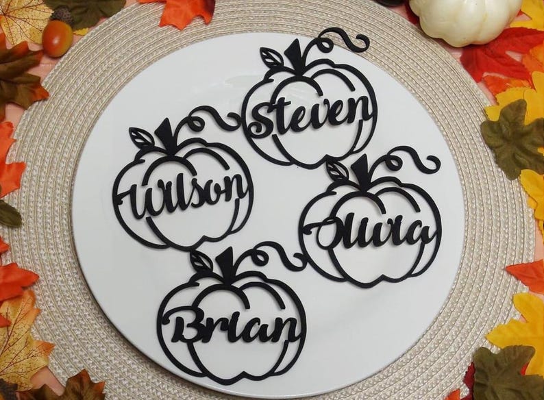 Puede incluir: Cuatro adornos negros con forma de calabaza cortados con l&aacute;ser en material plano. Cada calabaza tiene un nombre recortado en el centro: steven, Wilson, Olivia y Brian. Los adornos tienen tallos y zarcillos rizados en la parte superior.