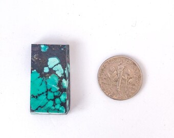 May include: A rectangular piece of turquoise stone with a dark green and black matrix. The stone is about the size of a US dime.