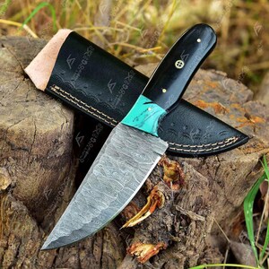 May include: A black and green handled knife with a Damascus steel blade. The knife is resting on a piece of wood with a leather sheath.