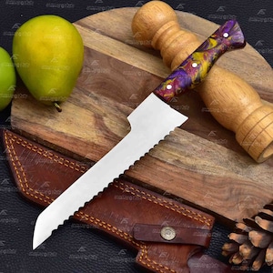 May include: A bread knife with a purple, yellow and red marbled handle. The knife has a serrated blade and is resting on a wooden chopping board. A leather sheath is also visible in the image.