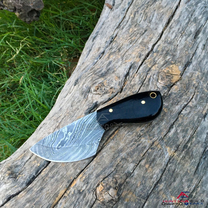 May include: A black handled knife with a Damascus steel blade. The blade is curved and has a pointed tip. The handle is made of black wood and has a brass pin.