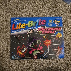 May include: A Lite-Brite picture refill featuring The Powerpuff Girls. The box is dark blue with the Lite-Brite logo and images of the characters. It includes 12 exciting pictures and is for ages 4 and up.