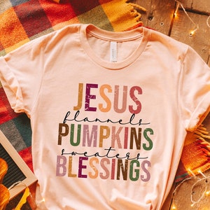 May include: A light pink t-shirt with the text "JESUS flannels PUMPKINS sweaters BLESSINGS" in colorful, distressed lettering.