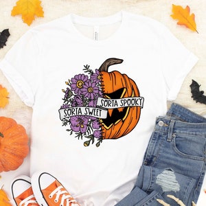 May include: White t-shirt with a graphic of a pumpkin with flowers on one side and a jack-o-lantern face on the other. The text "Sorta Sweet" and "Sorta Spooky" is on a banner around the pumpkin.