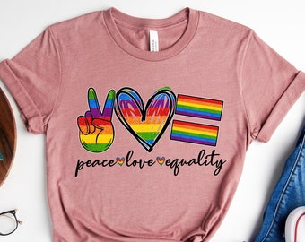 May include: A pink t-shirt with a peace sign, heart, and equality sign in rainbow colors. The text "peace love equality" is printed below the graphic.