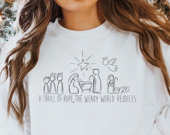 May include: White sweatshirt with a black illustration of the nativity scene and the text "A thrill of hope, the weary world rejoices".