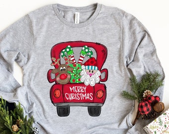 May include: A grey long-sleeved shirt with a red truck design featuring Santa, a reindeer, and a gift. The truck has the words "Merry Christmas" printed on the back.