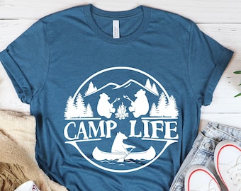 May include: A teal blue t-shirt with a white graphic design of two bears sitting by a campfire in a canoe with the text "Camp Life" in a circle around them.