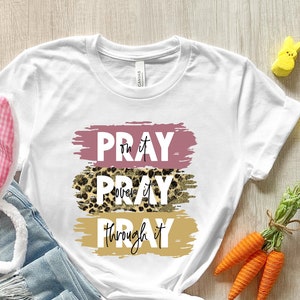 May include: White t-shirt with the text "Pray over it Pray through it" in pink, leopard print, and gold paint strokes.