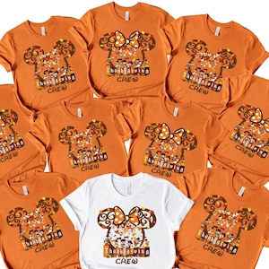 May include: A collection of orange and white t-shirts featuring a Thanksgiving-themed design. The design includes a Mickey Mouse head with a bow, fall leaves, and the words "Thanksgiving Crew".