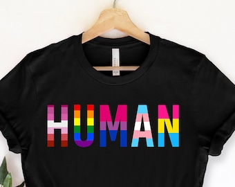 May include: Black t-shirt with the word "HUMAN" printed in rainbow colors, including the transgender flag colors.