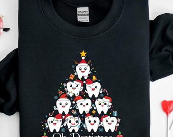Könnte beinhalten: Schwarzes Sweatshirt mit einem Weihnachtsbaum-Design aus lächelnden Zähnen, die Weihnachtsmützen und festliche Dekorationen tragen. Der Text "Oh Dentistree" ist unten aufgedruckt. Ein lustiges Design zum Thema Feiertage für Zahnärzte.