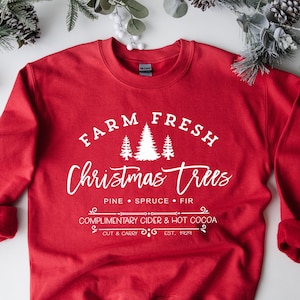 May include: Red sweatshirt with white text that reads "FARM FRESH Christmas trees PINE SPRUCE FIR COMPLIMENTARY CIDER & HOT COCOA CUT & CARRY EST. 1929".