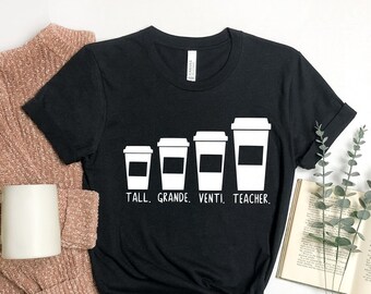 May include: Black t-shirt with a white graphic of four coffee cups in different sizes. The text "Tall. Grande. Venti. Teacher." is printed below the cups.