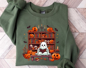 Może przedstawiać: Zielona bluza z nadrukiem ducha czytającego książkę w biblioteczce wypełnionej dyniami i świecami. Biblioteczka jest ozdobiona nietoperzami i gwiazdami.