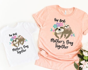May include: Two white t-shirts with a sloth design and the text "Our first Mother's Day Together". The larger shirt is peach colored.
